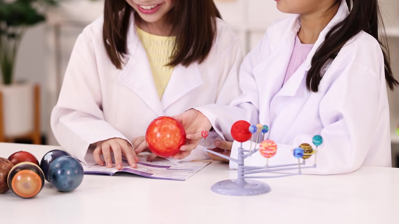 教室で白い白衣を着た2人の若いアジア人学生が惑星モデルを調べている。