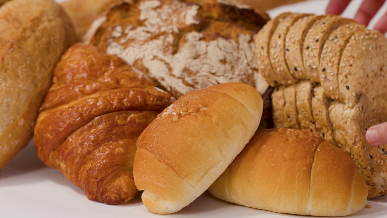Close-up of hands picking sliced bread from a variety of fresh croissants and baguettes.