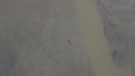 Overhead-top-down-aerial-view-of-tiny-fishing-boat-in-middle-of-brown-river