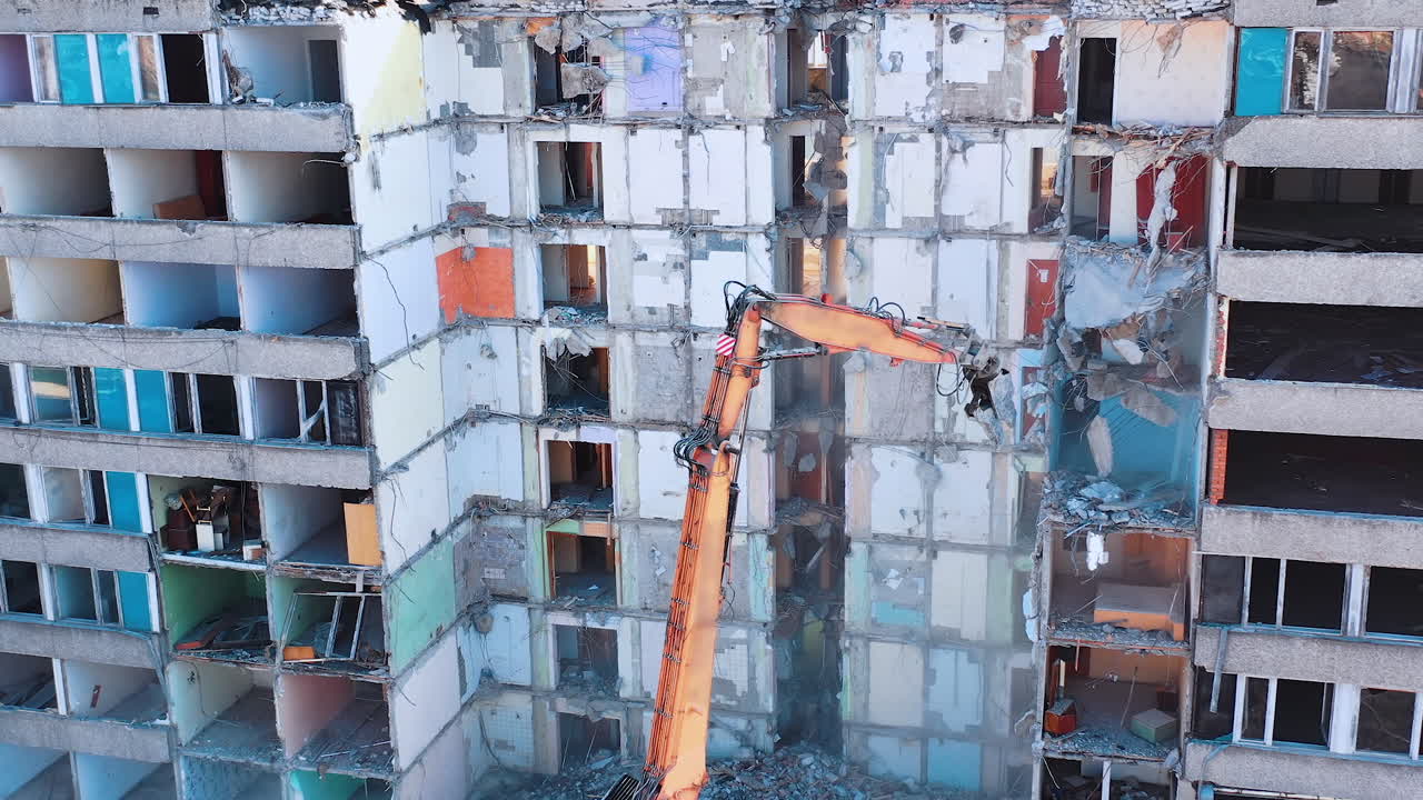 Excavator grabber reaches high to dismantle the walls of an old building. Parts of concrete and heavy dust falling down. Construction excavators are clearing the ruins of an old building.