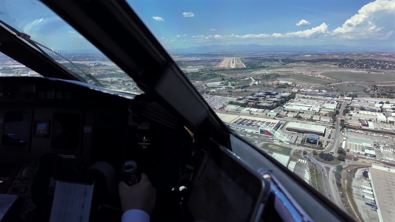 Pemandangan pilot imersif melalui kaca depan kokpit saat mendekati landasan pacu 32R Bandara Madrid, dengan pemandangan tangan kopilot di kendali, dan landasan pacu di depan di bawah langit biru dengan sedikit awan.