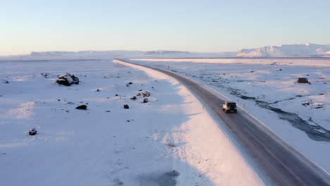 Antena:-Paisaje-Blanco-Como-La-Nieve-Con-Carretera-Siguiendo-Jeep-En-Islandia-Al-Atardecer-Invierno,-Sol,-ártico