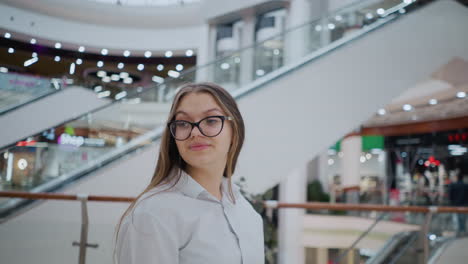 elegant lady with glasses walking in a modern shopping mall glances back with curiosity, she wears a stylish white blouse, and the background