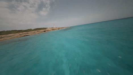 FPV-Drohnenaufnahme-über-Einer-Atemberaubenden-Landschaft-Mit-Wunderschönem-Türkisfarbenem-Meerwasser-Entlang-Eines-Felsigen-Strandes-Mit-Leuchtturm-über-Dem-Strand