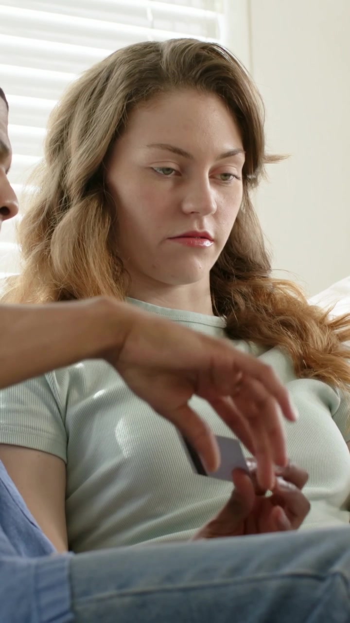 Vertikal video: En mann kommer inn og lener seg mot en kvinne i mintfarget t-skjorte på sofaen, og berører fanget hennes.
