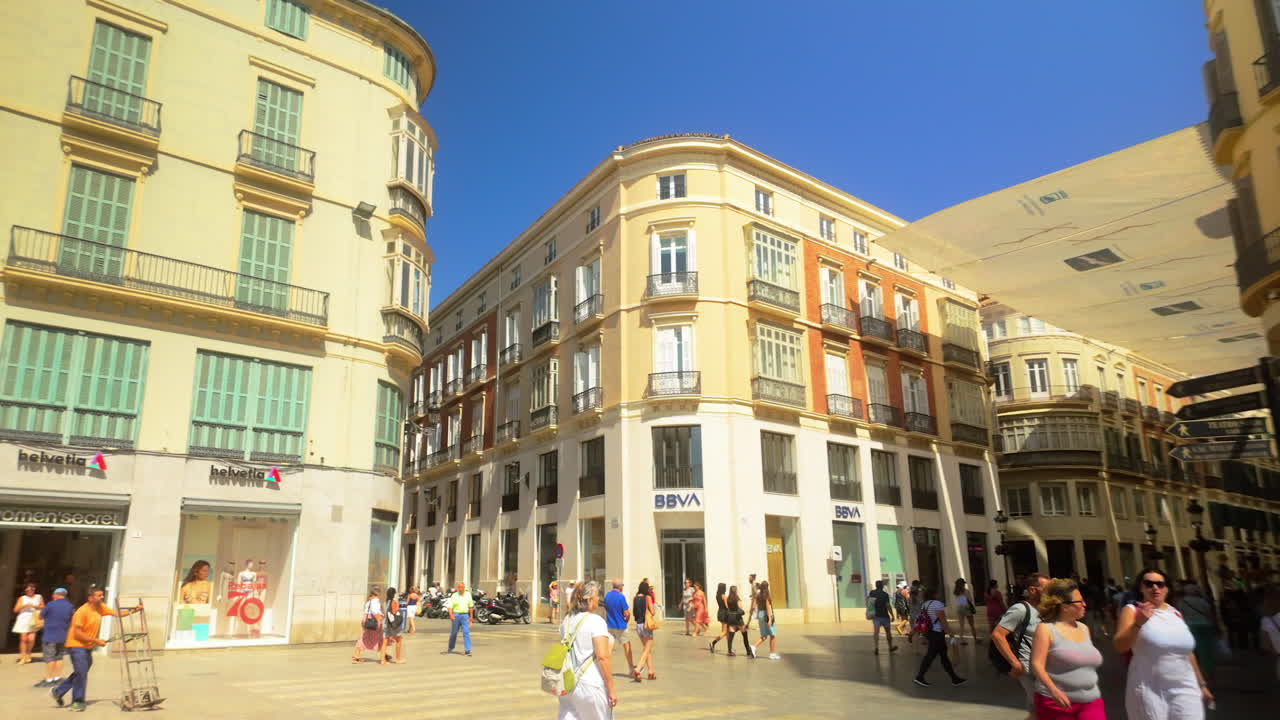 Street view of historic European buildings in Málaga's city center, with people walking and shopping on a sunny day