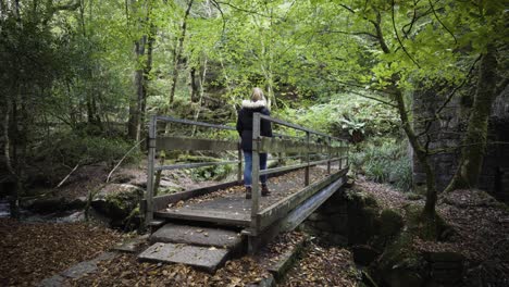 Mujer-Solitaria-Cruzando-Un-Viejo-Puente-En-La-Reserva-Natural-De-Kennall-Vale-En-Ponsanooth,-Inglaterra