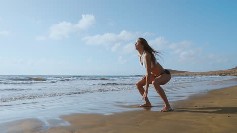 Una-Chica-Con-Pantalones-Cortos-Y-Camiseta-Deportiva-Realiza-Saltos-Con-Sentadillas-Y-Aplausos-En-La-Playa-Cerca-Del-Océano-En-Las-Islas-Canarias.-Estilo-De-Vida-Saludable-Y-Fitness-Durante-Las-Vacaciones.-Cuerpo-Hermoso-Y-Saludable