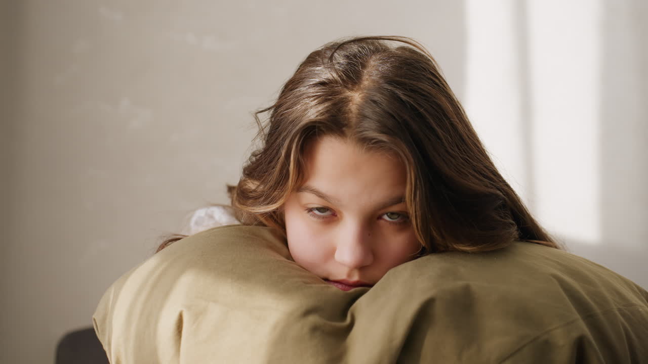 Teenager Calmly Hugging Pillow Indoors, Thoughtful Teen Greets Pillow In Peacefully Lit Living Space, Serene Young Person Embracing Cushion While Gazing Contemplatively In Bright Home Setting