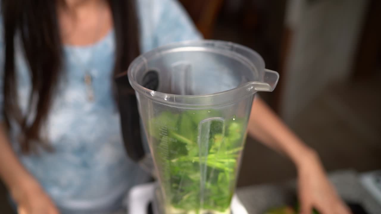 여자가 믹서기에 녹색 채소를 넣고 있다