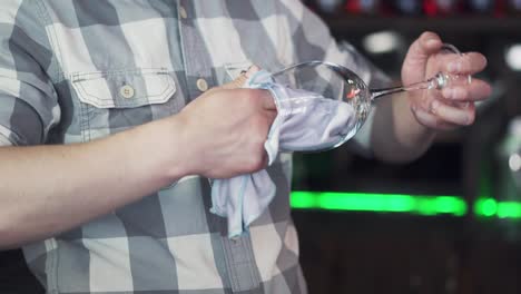 male barman is wiping a wet glass with dry napkin on the bar background. bartender polishes a glass near the counter