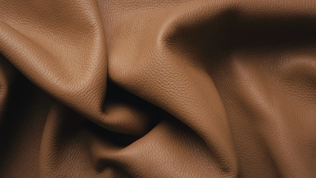 Top down view of a brown leather hide being folded open on a table in a leather workshop. 4K