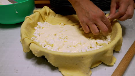 Woman-sets-up-a-cheese-pie-in-oven-pan,-forming-dough,-close-up-on-hands-4K