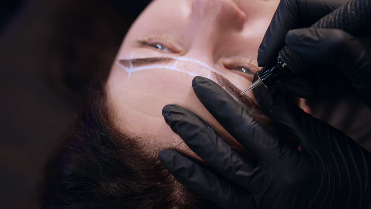 Tattooist makes permanent eyebrow make up. Woman having cosmetology procedure in salon. Close up.