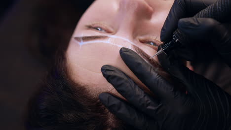 tattooist makes permanent eyebrow make up. woman having cosmetology procedure in salon. close up.