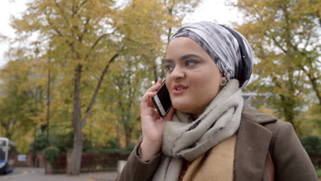 british muslim woman using mobile phone in park