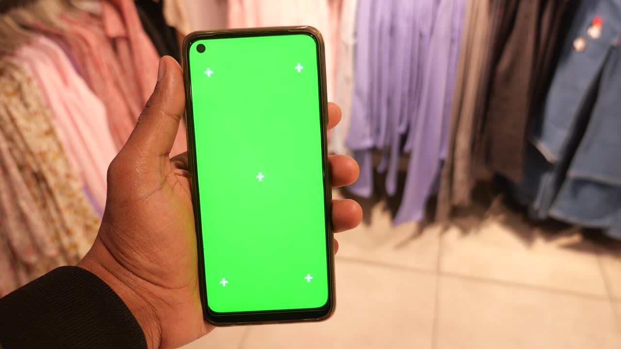 persona con un teléfono inteligente de pantalla verde en una tienda de ropa