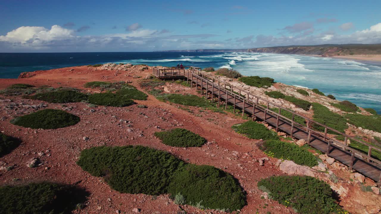 포르투갈 알가르베 지역의 보르데이라 모래 해변에서 서핑을위한 완벽한 파도가있는 그림 같은 해변의 파노라마 뷰를 즐기는 커플.