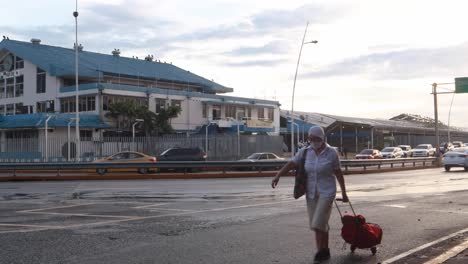 Panama-Citys-Fischmarkt-In-Der-Nähe-Der-Nassen-Asphaltstraßen-Der-Balboa-Avenue,-Wo-Bürger-In-Fahrzeugen-Von-Und-Zu-Ihrem-Arbeitsplatz-Fahren-Und-Eine-Dame-Mit-Gesichtsmaske-Eine-Tasche-über-Den-Rahmen-Rollt