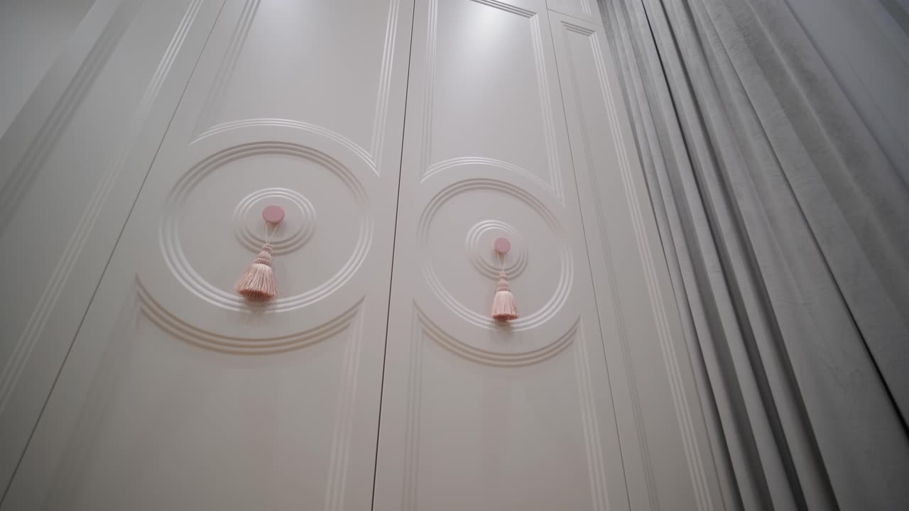 пара двойных дверей в классическом стиле, украшенных декоративными ручками, установленных в изысканном интерьере с сложными облицовками и мягкими занавесками.