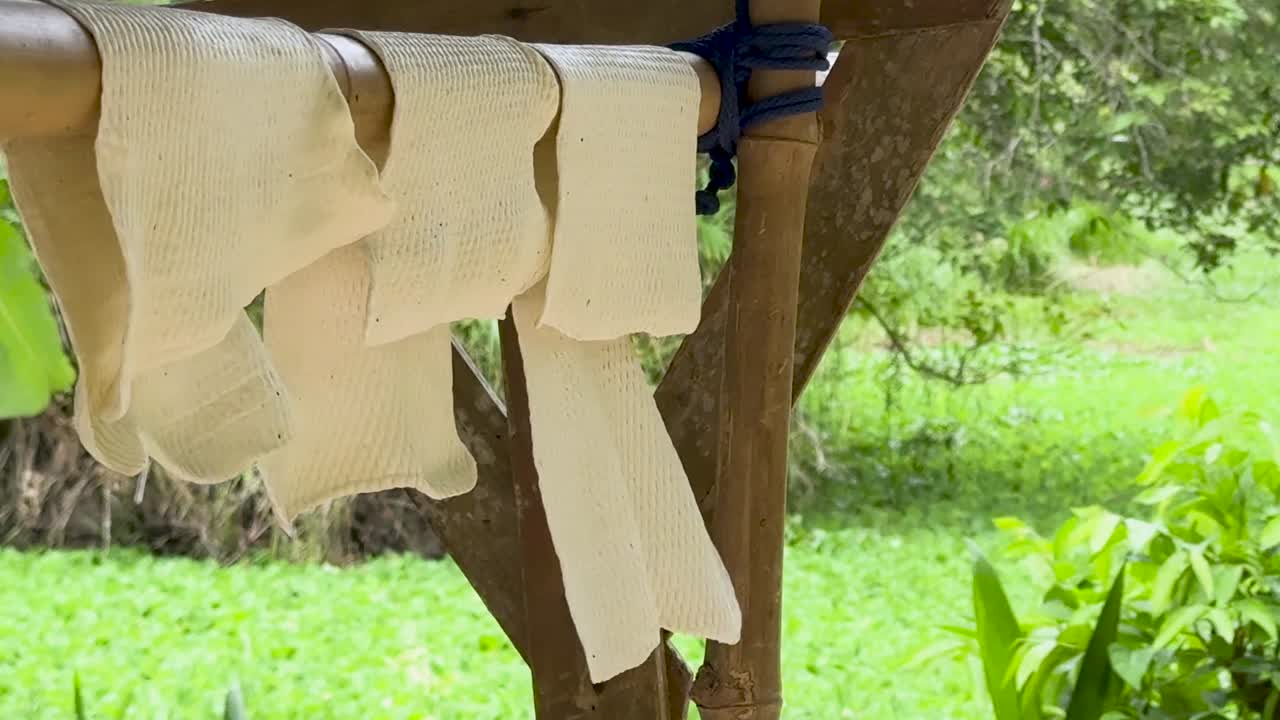 Close-up of white rubber sheets hanging to dry on a wooden structure in tropical sunlight
