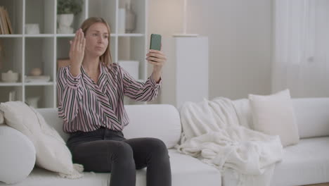 young woman is chatting by video call in cellphone sitting at home and communicating with friends during self-isolation