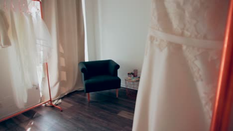 showing atmospheric beautiful preparation room for brides with copper stands and wedding dresses hanging in shop, grey chair modern style