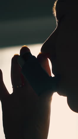 cu: dark silhouette of young woman using inhaler to relief asthma symptom against backlight in room extreme close view