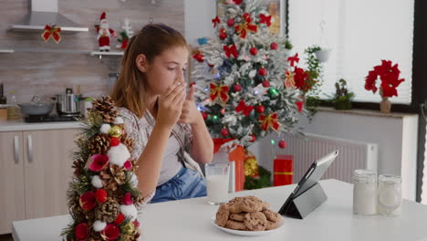 niño feliz sentado en la mesa en la cocina decorada viendo video en línea de xmas en una tableta