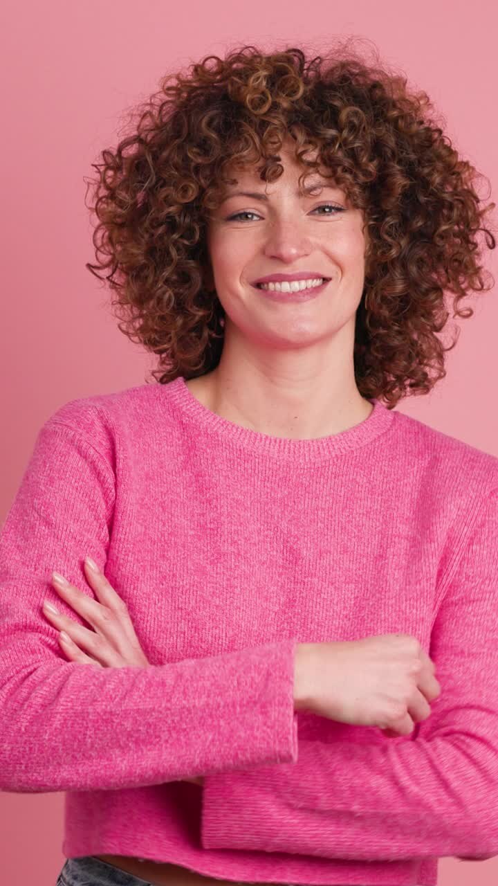 Smiling standing young curly haired woman on pink background. Vertical footage
