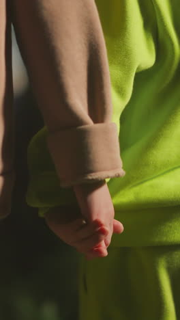 elder sister holds younger brother hand while standing in evening garden. little boy and girl dressed in comfortable sports suits spend time together having fun