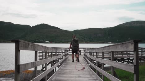 male backpacker with pet dog on leash walking on wooden walkway by the lake shore