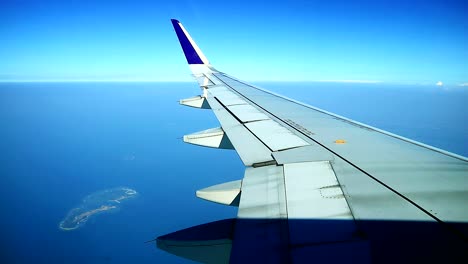 Vista-De-Una-Pequeña-Isla-En-Medio-Del-Océano-Desde-Las-Ventanas-De-La-Cabina-Del-Avión