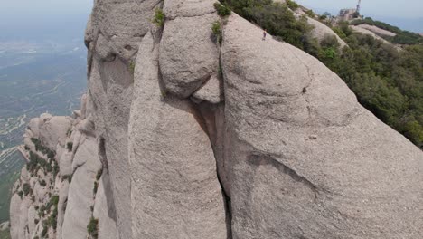 aerial shot of a man standing on the rock of the unique mountains surrounding the monestary of montserrat, aerial footage in spain, europe