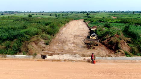 Uso-De-Equipo-Pesado-De-Carga-Frontal-En-Nigeria-Para-Despejar-La-Vegetación-Para-La-Construcción-De-Carreteras---Vista-Aérea-Deslizante