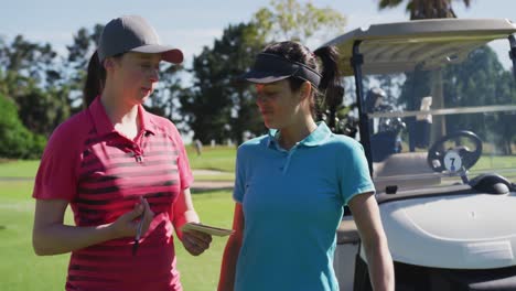 Two-caucasian-women-playing-golf-talking-writing-in-notebook