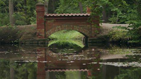 red brick built arch footbridge in parkland waterlily pond setting