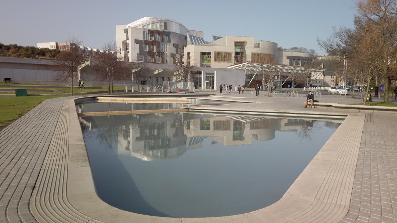 Panorámica ascendente desde un pequeño estanque frente al edificio del Parlamento Escocés en Holyrood en un día soleado, Edimburgo, Escocia.