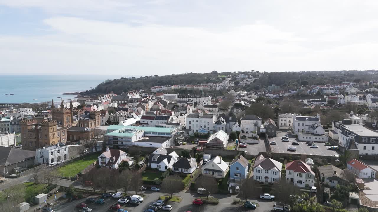 vuelo sobre los techos de st peter port guernsey hacia el colegio elizabeth con vistas al mar y el promontorio boscoso más allá en un día brillante