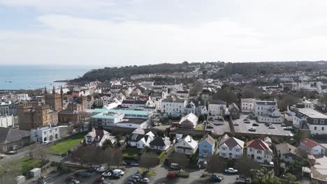 flight over roof tops of st peter port guernsey towards elizabeth college with sea views and wooded headland beyond on bright day