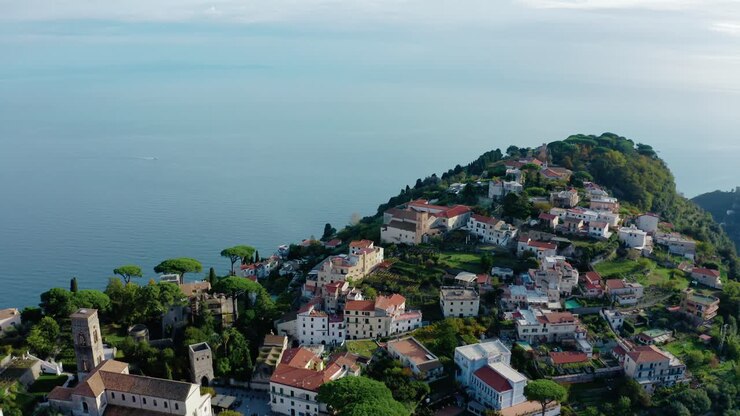 Vista aerea con drone della città di Ravello, arroccata in alto sopra il Mar Mediterraneo in Costiera Amalfitana. Storica città italiana a picco sulla scogliera in un paesaggio montano mozzafiato. Volo verso il punto panoramico della Terrazza dell'Infinito.