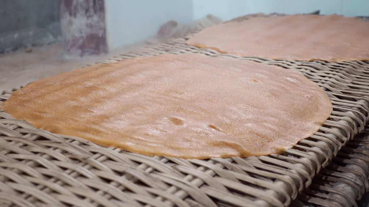extendiendo masa cruda caliente de un postre vietnamita en una bandeja de mimbre