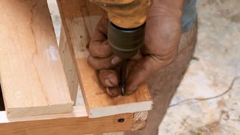 skillfull carpenter employing a power drill to attaching screws into a small wooden chair in his small business workshop to sell and support the local economy