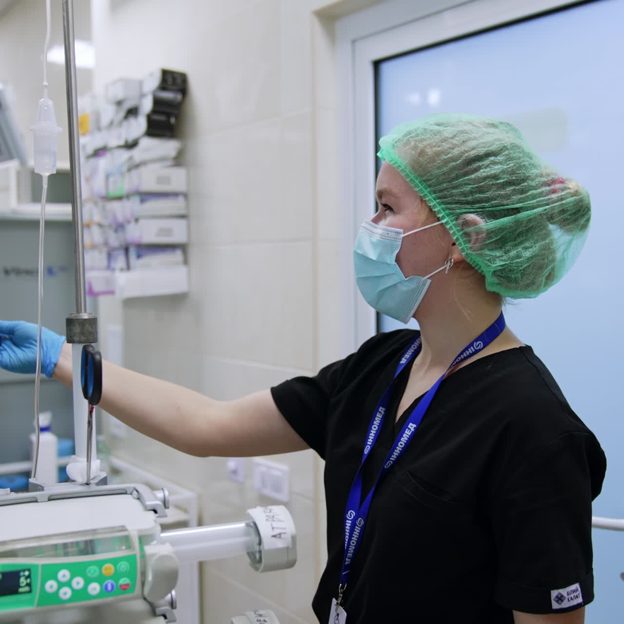 Smiling female nurse is in the modern surgery room. Medic in black uniform touches the screen of lung ventilator machine