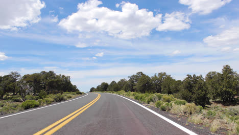 slow motion pov shot from a car driving down a windy country road in flagstaff ariozna on a sunny day with clouds overhead