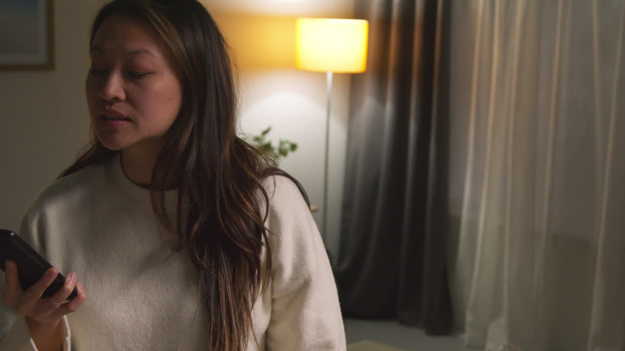 화를 내고 불안하거나 스트레스를 받는 여성이 집에서 휴대전화로 대화하는 라운지에서 저녁을 보내고 있습니다.