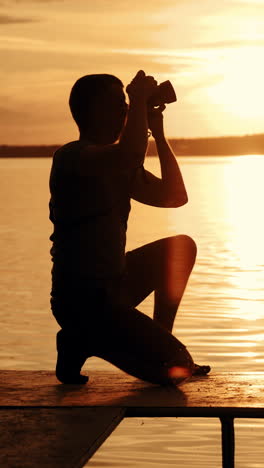 a young photographer was squatting and photographing the sunset on the bridge of the river near bench after which he left that place. vertical video