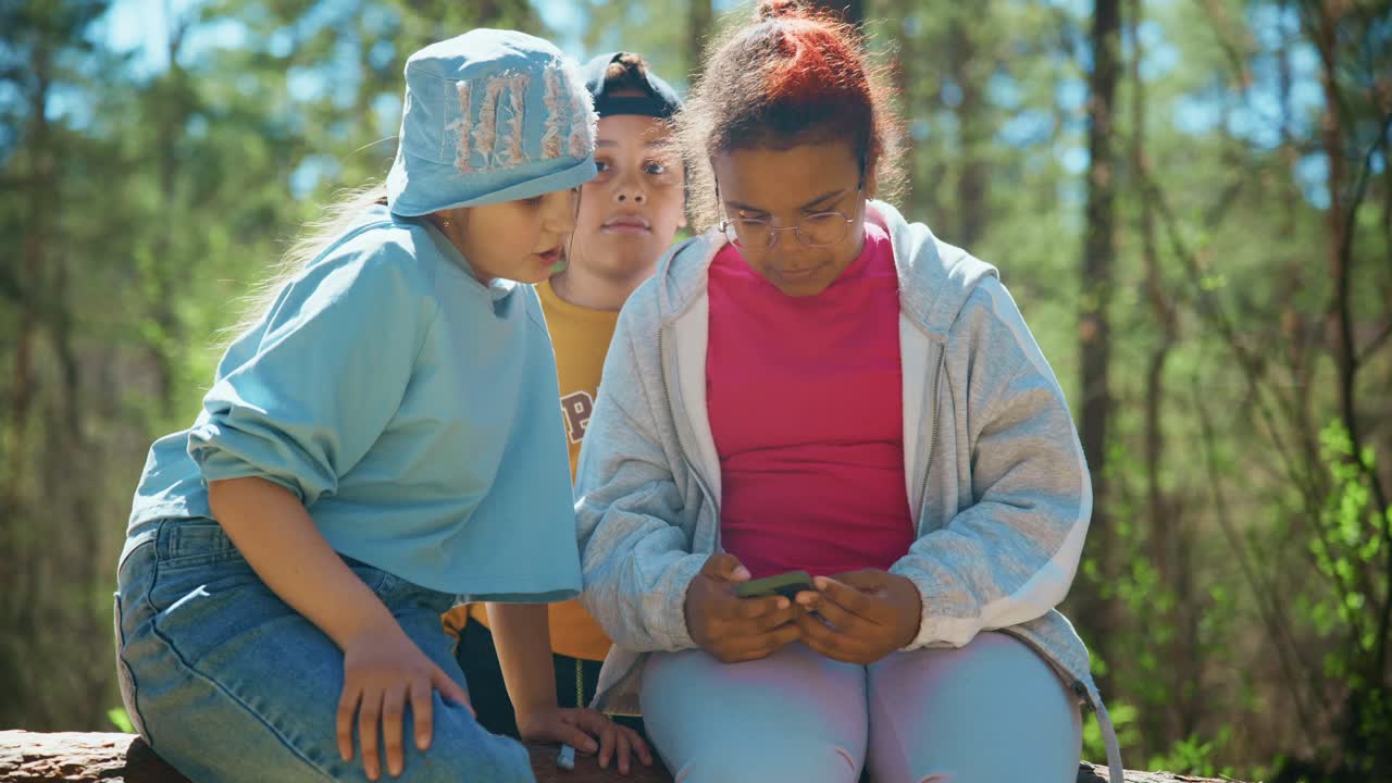 Three Girls Looking at a Smartphone in a Forest