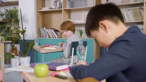 ginger male student writing on a paper during class, then looking at his classmate and smiling