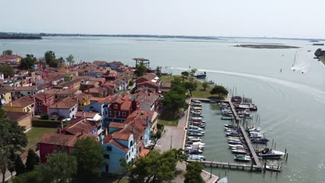 backwards drone flight in 4k over the harbour of the small island of burano venice italy with boats and houses and horizon